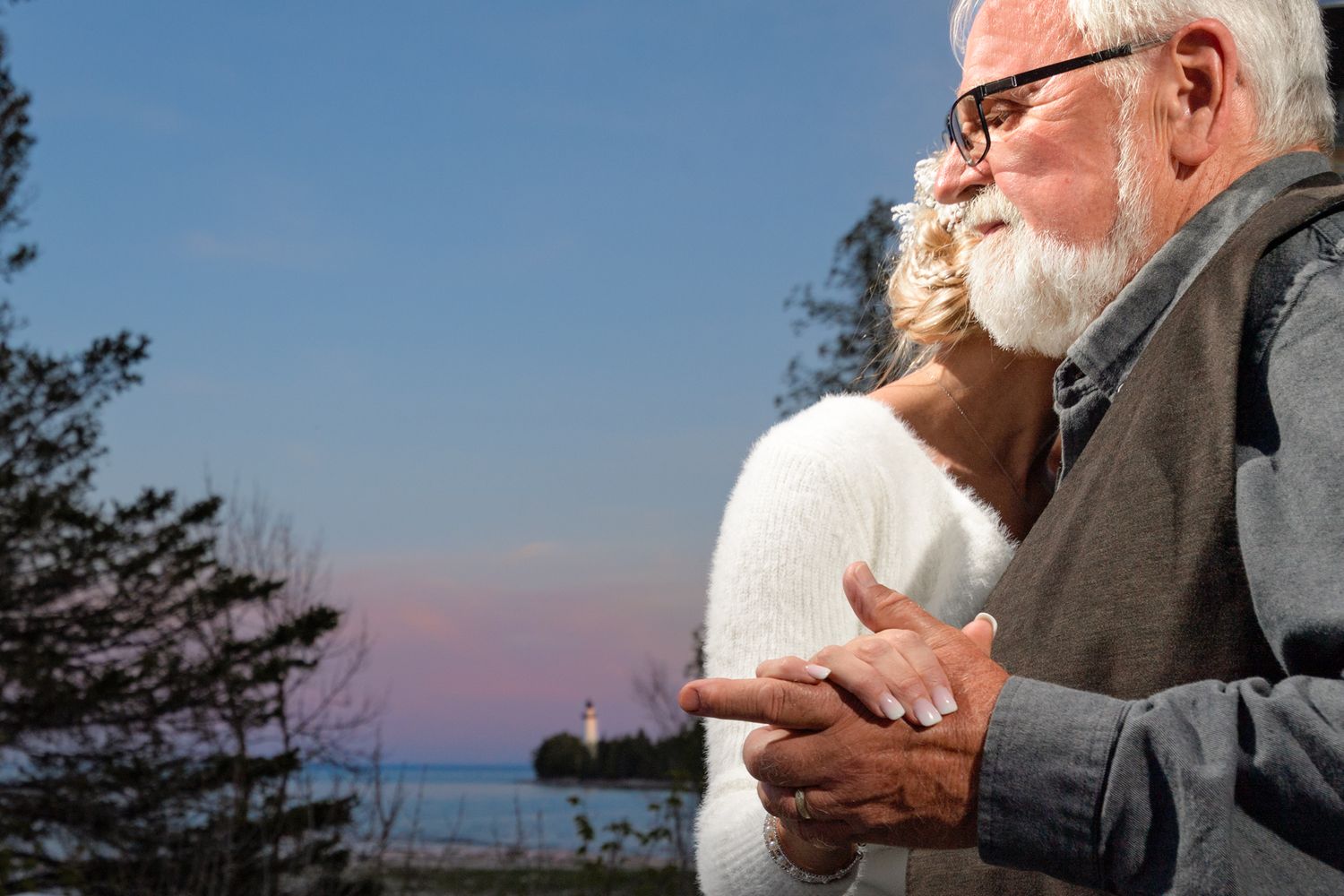 A touching moment at sunset on a deck overlooking a scenic lake view with evergreen trees.