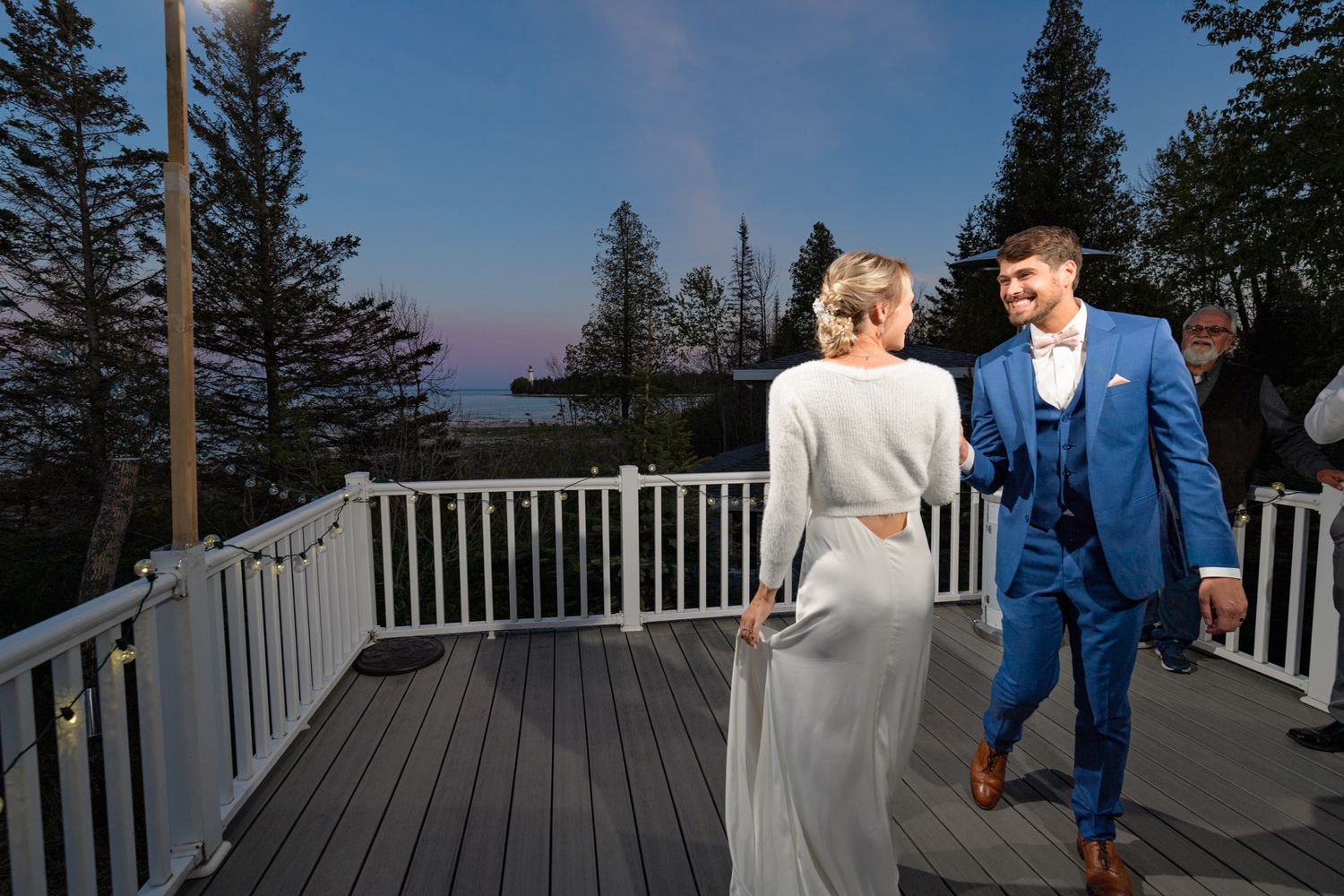 Dancing together on a deck at twilight with pine trees and lake views in the background.