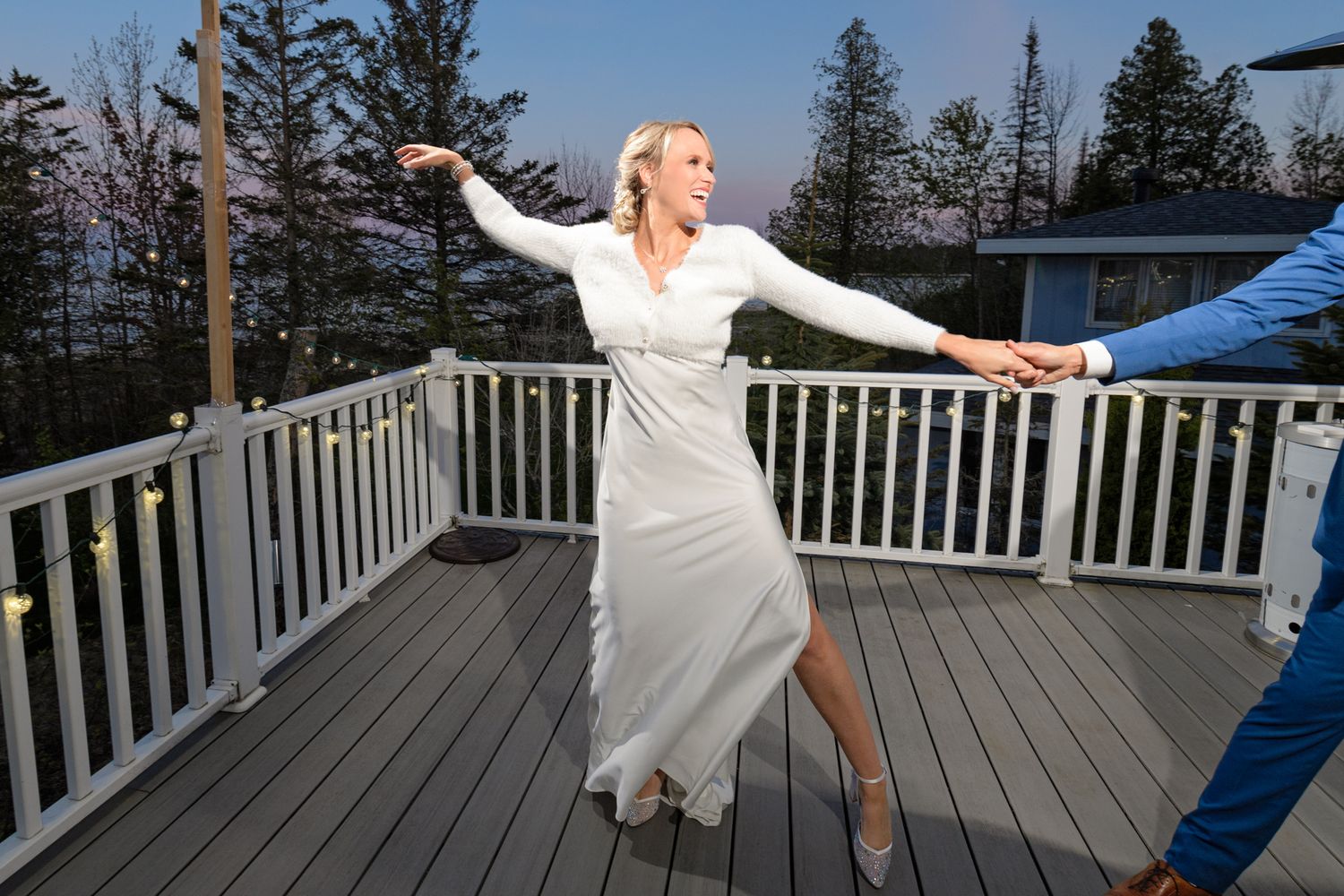 Joyful dancing on a wooden deck with white railings and evergreen trees in the background.