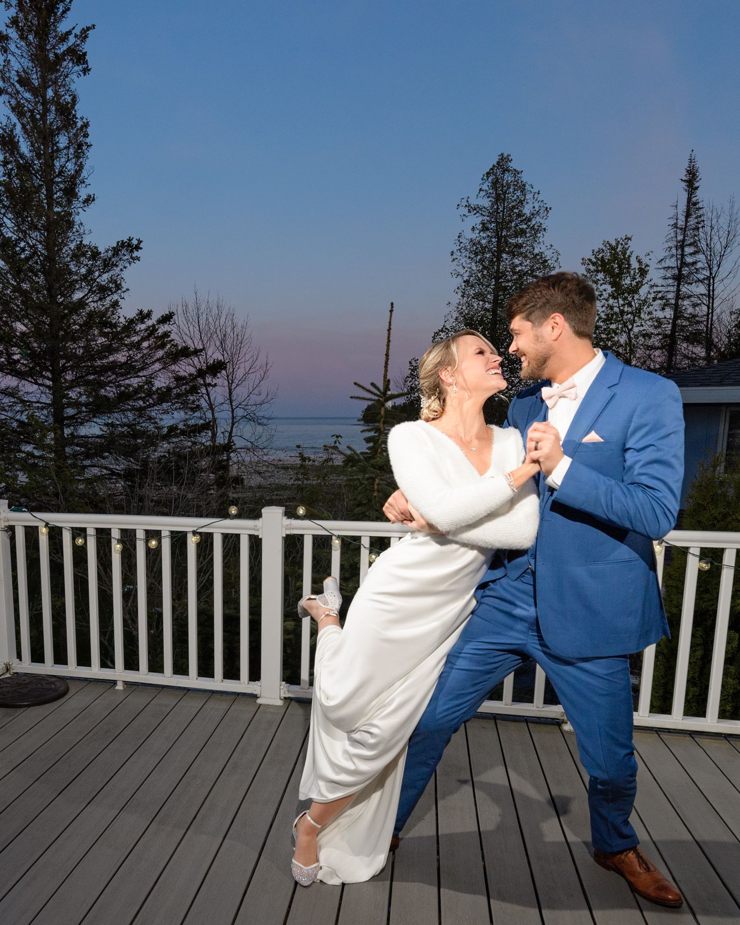 A romantic dance moment on a deck overlooking a scenic forest landscape at dusk.