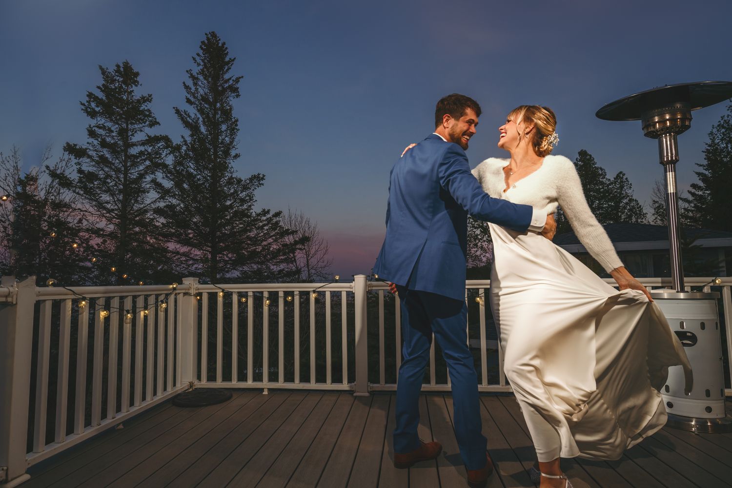A romantic sunset dance on a wooden deck surrounded by pine trees and white railings.