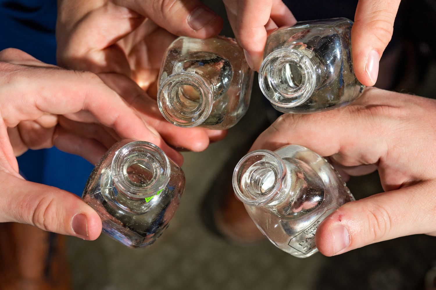 Hands toasting with four clear glass shot glasses in a circle.