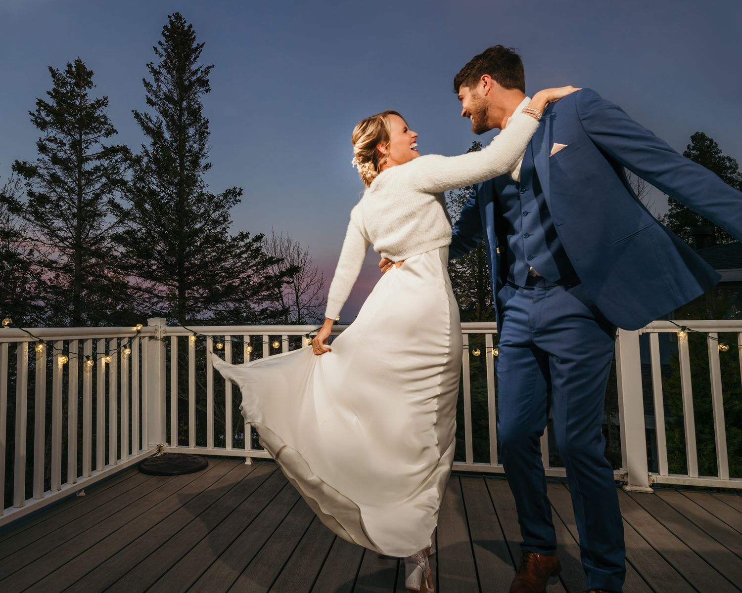 A dramatic dance pose captured on an outdoor deck with scenic forest backdrop at dusk.