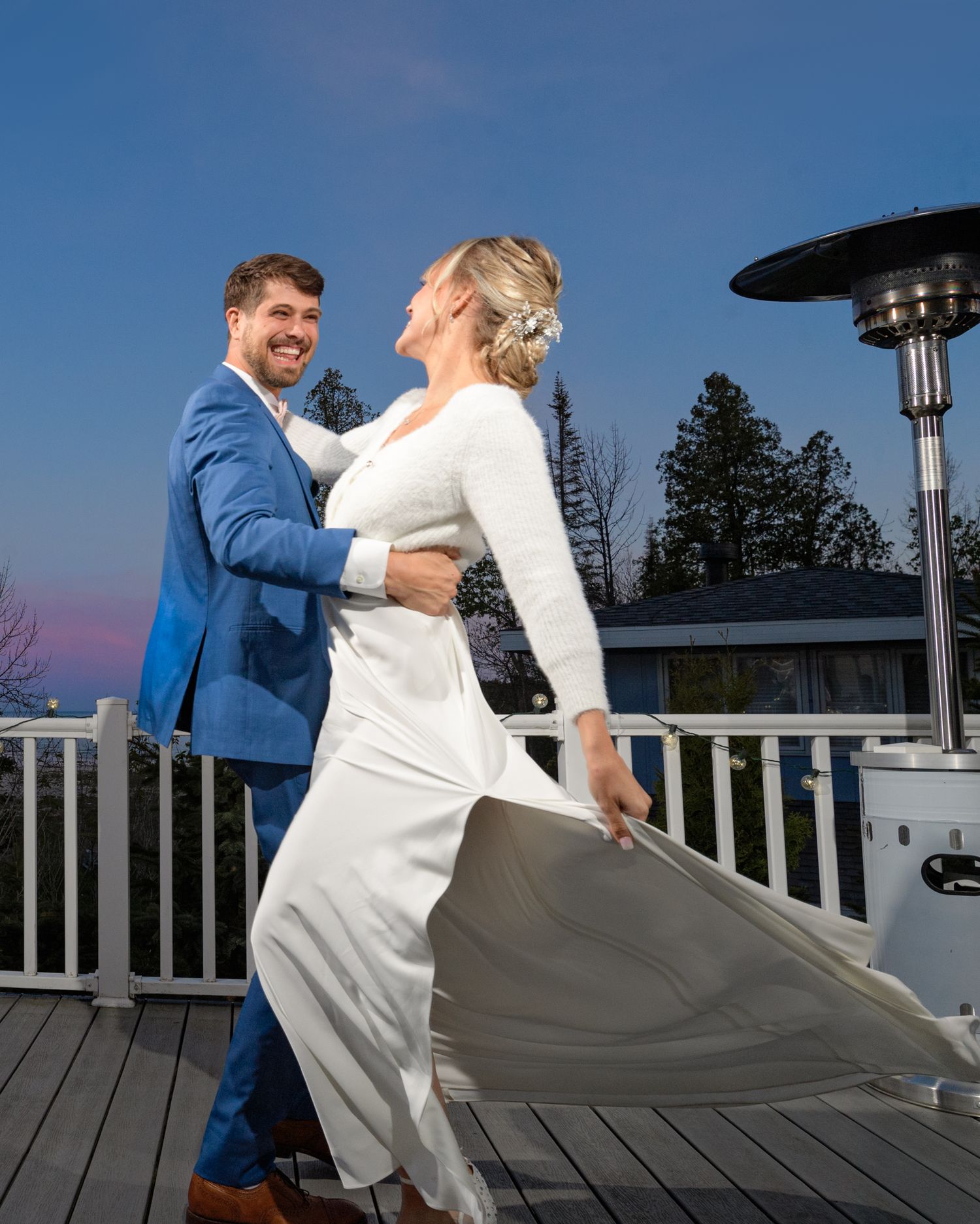 A joyful dance moment captured on a deck with outdoor heater and pine trees in background.