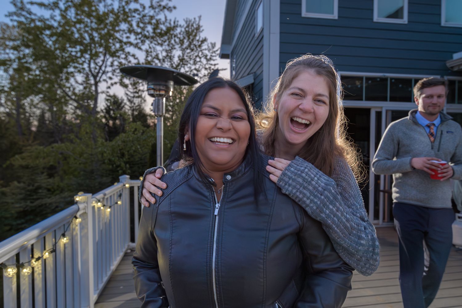 Friends sharing a joyful moment and laughing together on an outdoor deck at dusk.