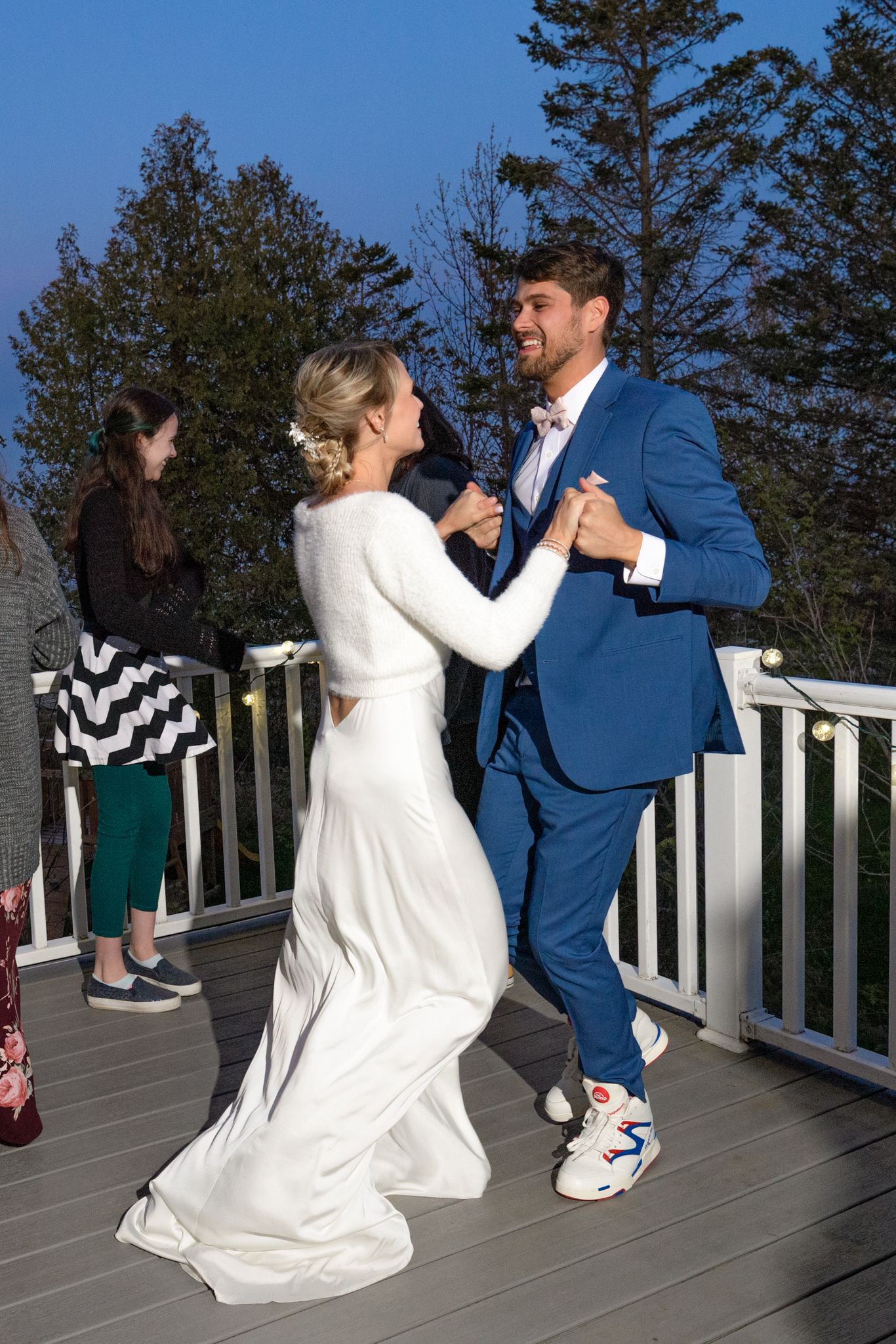 Dancing couple in formal attire on deck with sneakers and pine trees in background.