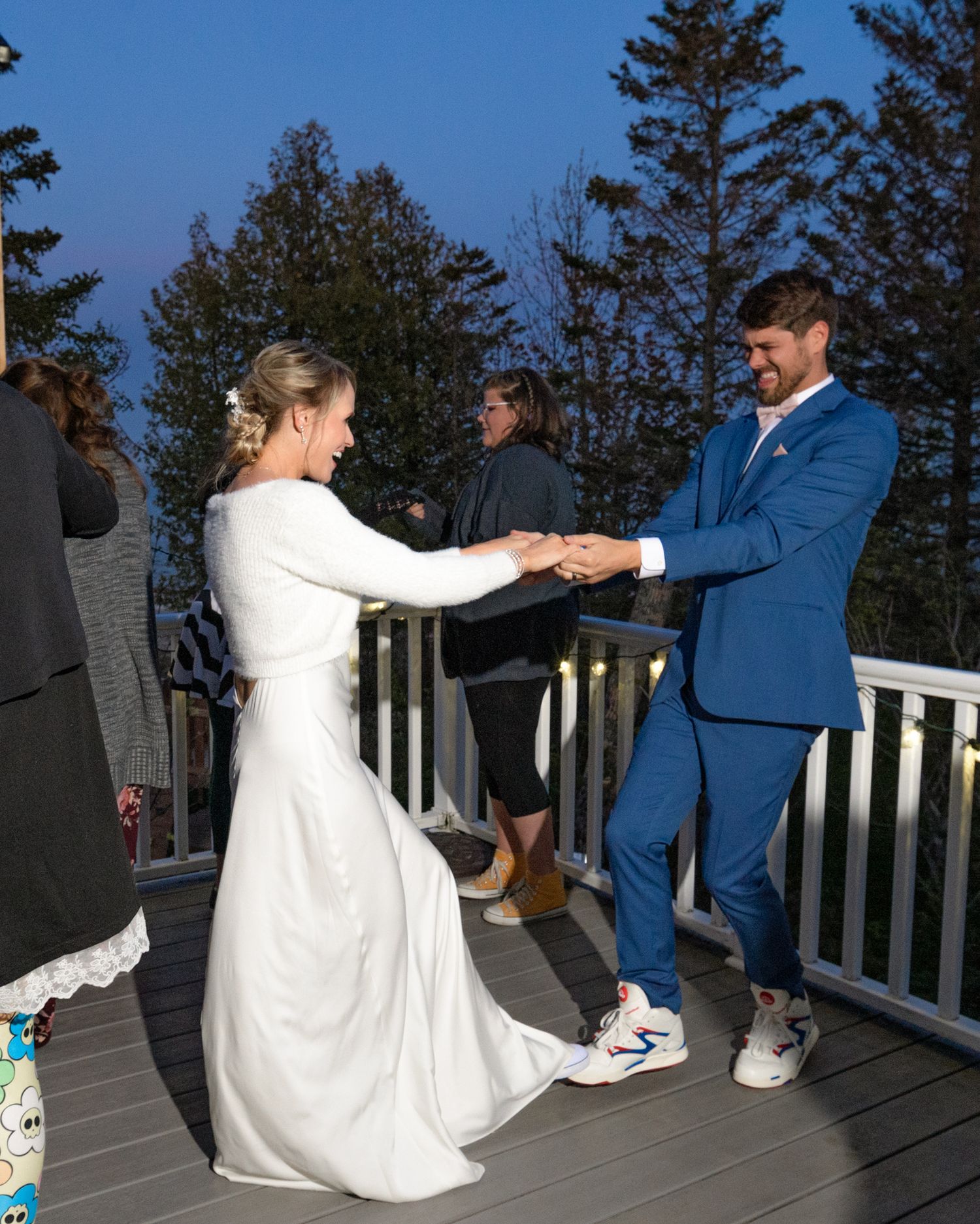 Couple dancing together on wooden deck with evergreen trees in background.