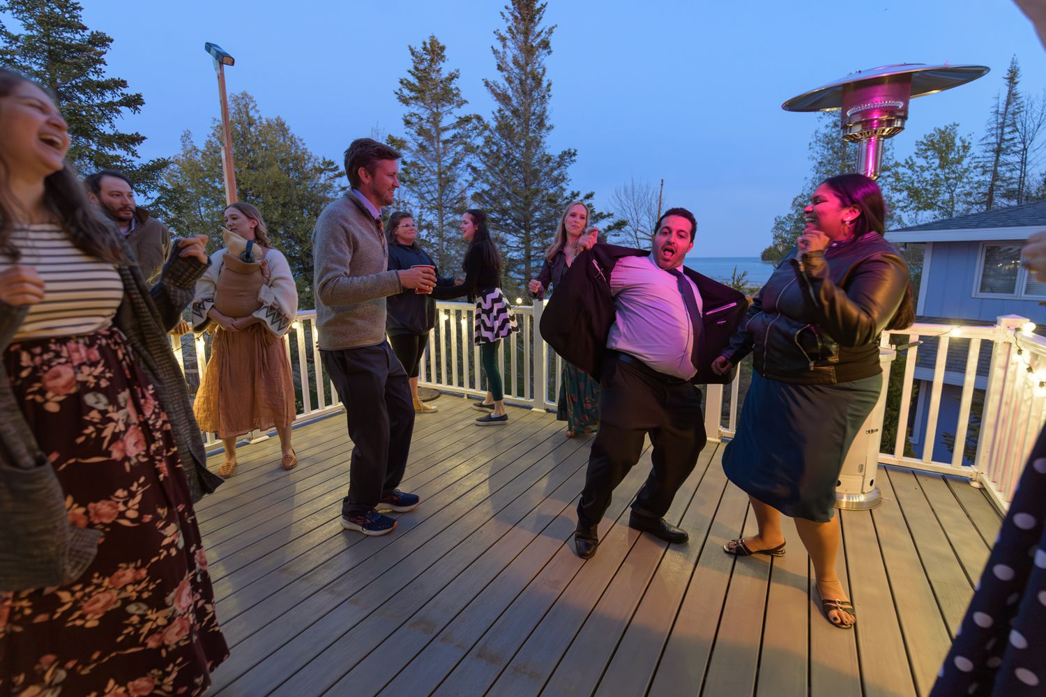 Group of wedding guests dancing on illuminated deck during evening celebration.