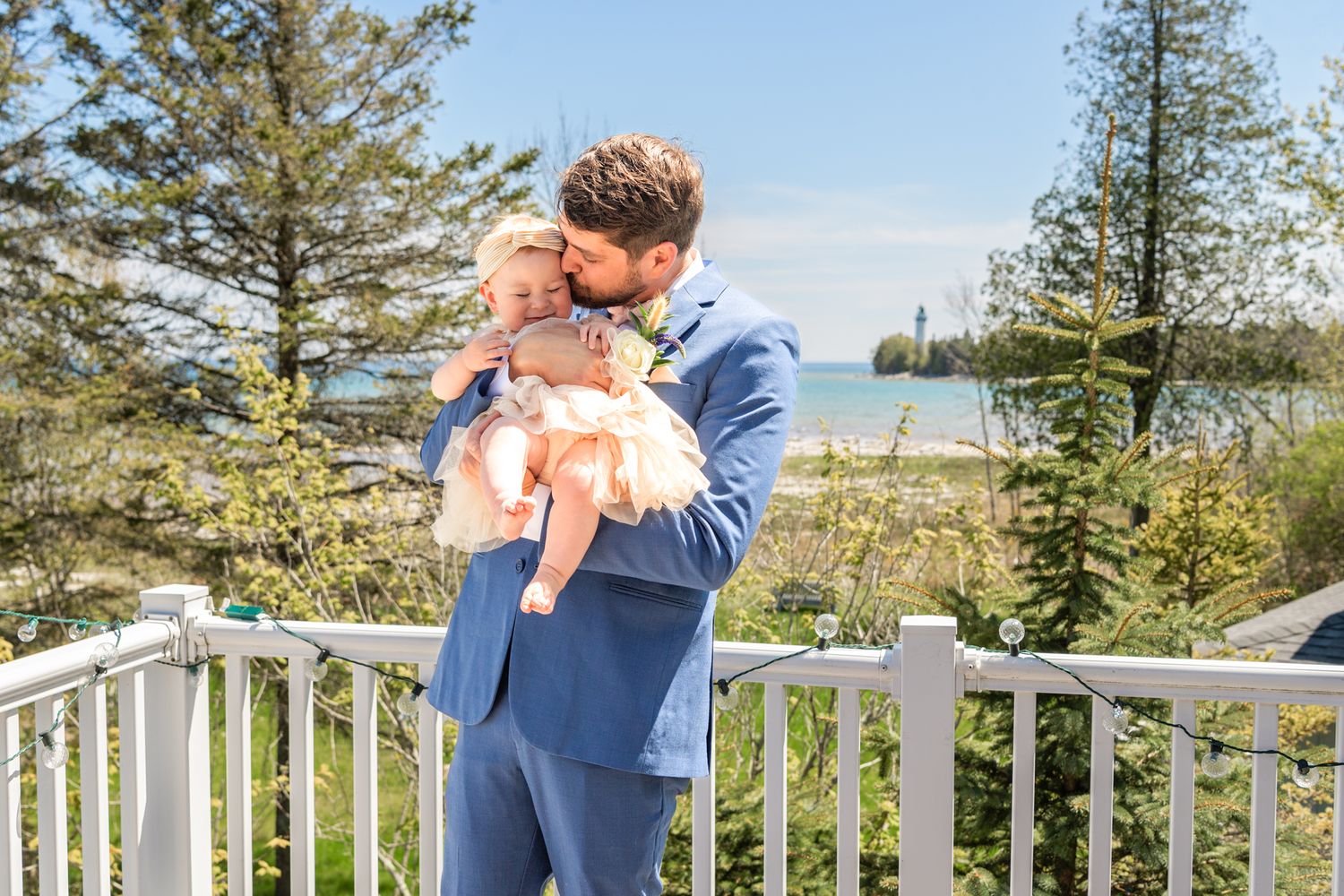 A couple shares an intimate moment on a deck with evergreen trees and water in the background.