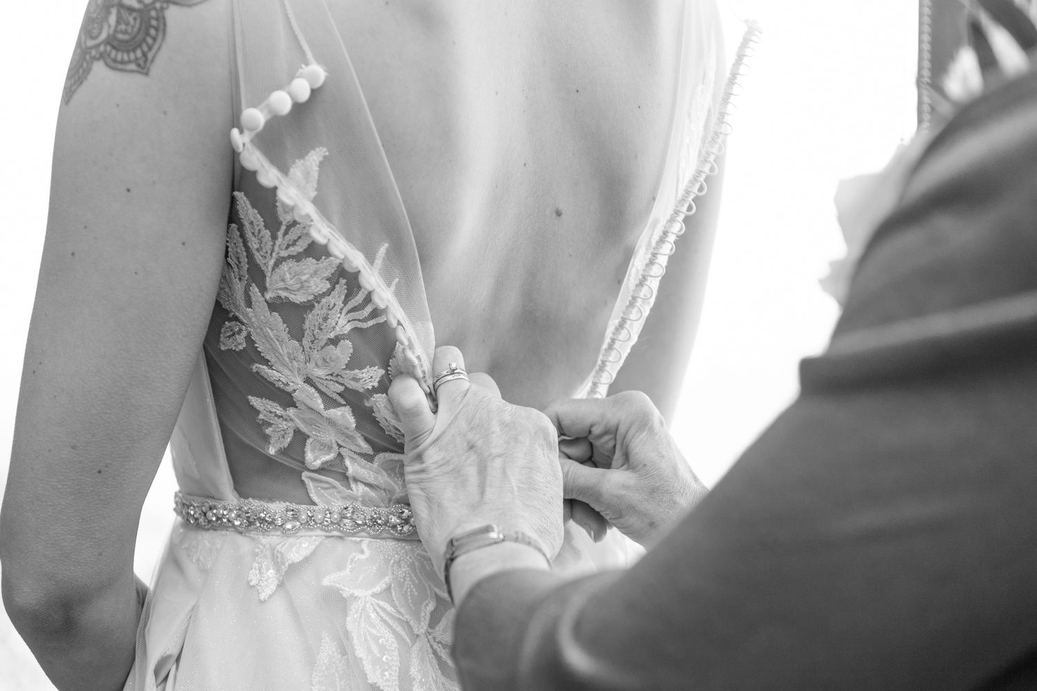 Close-up black and white shot of buttons being fastened on an ornate wedding dress.