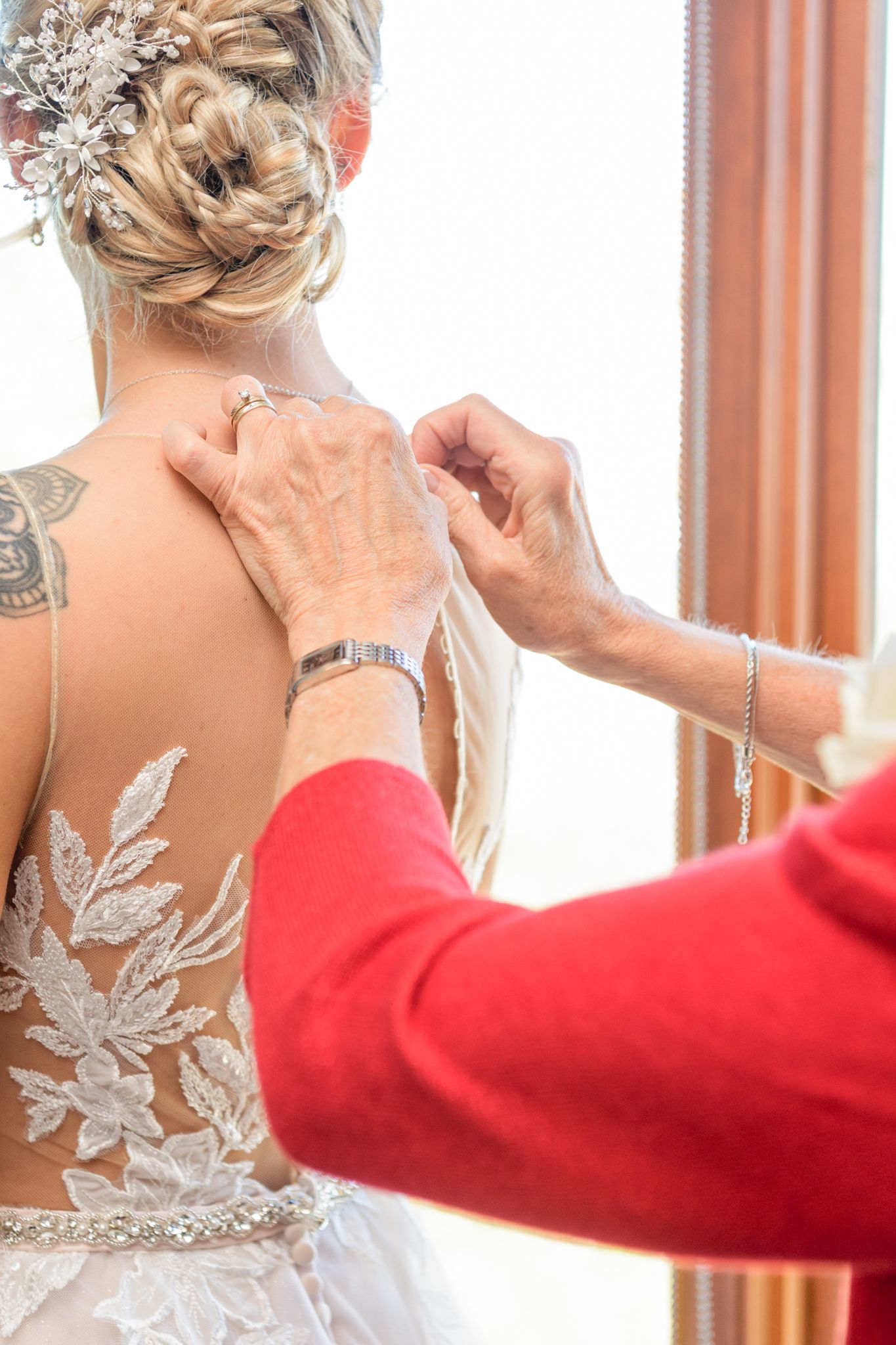 Detailed shot of hands fastening an intricate lace wedding dress with floral appliques.