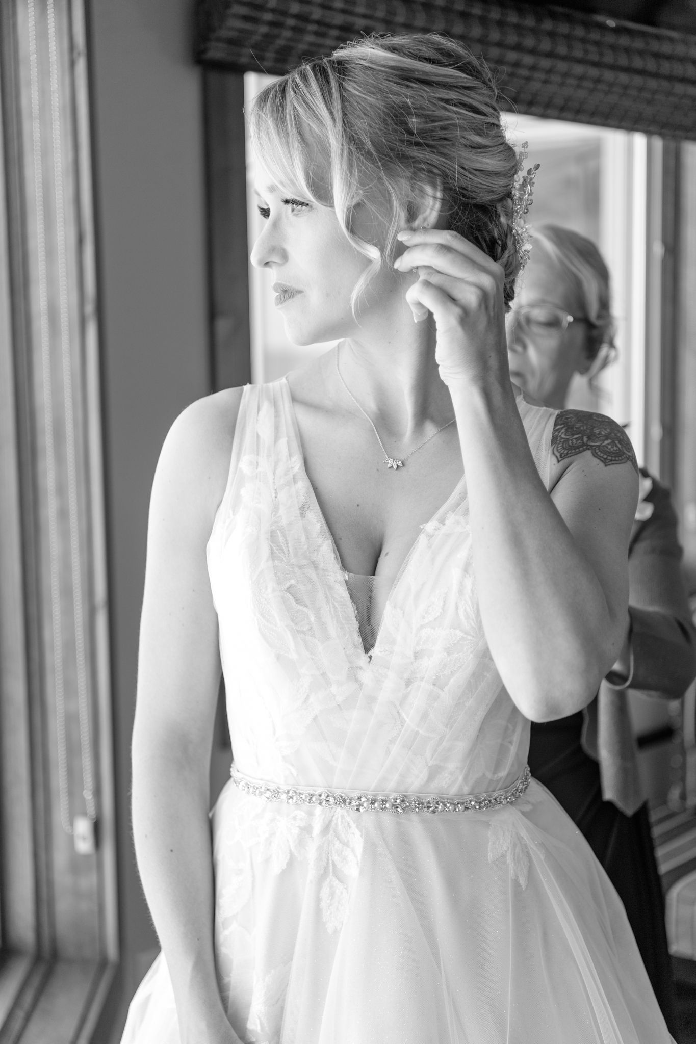 A bride in a white dress adjusts her earring while getting ready.