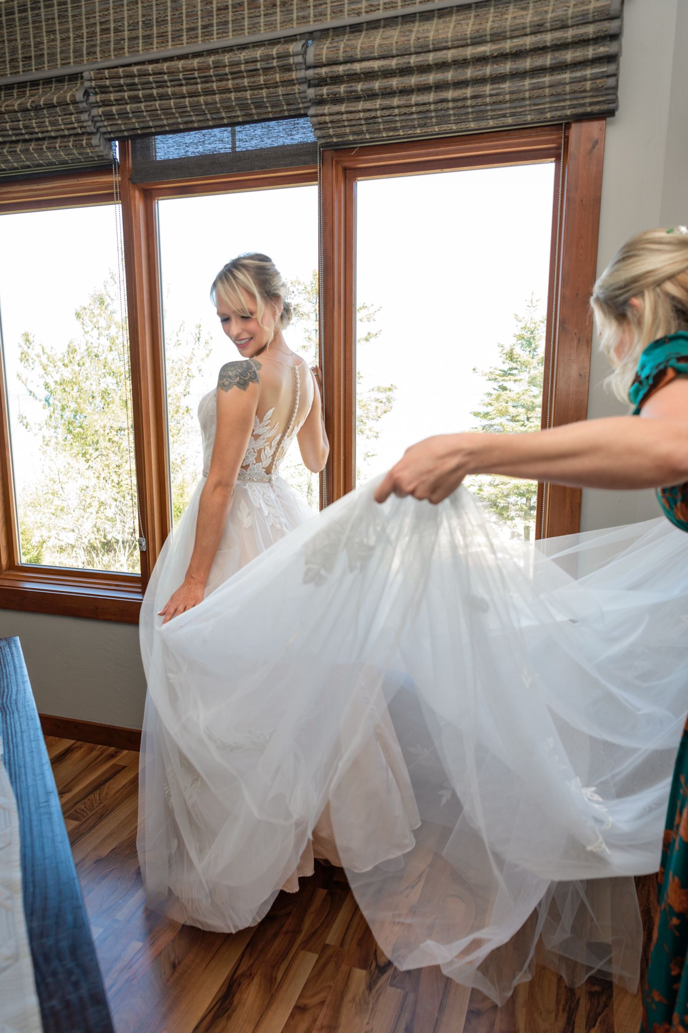 Wedding dress being adjusted from behind to show full tulle skirt near large windows.