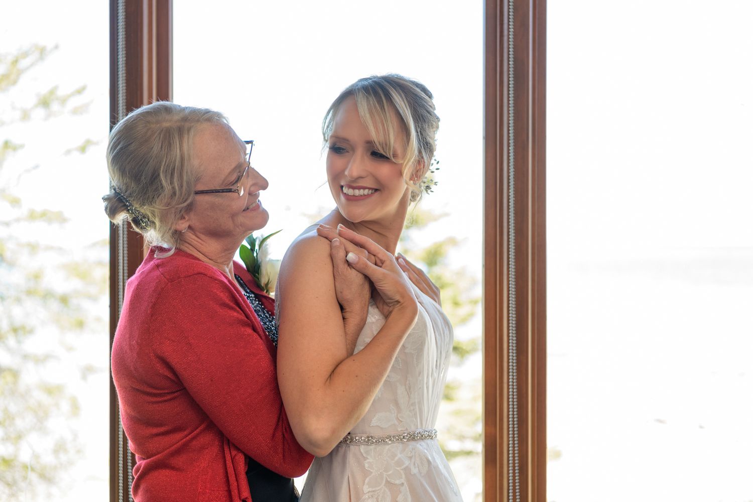 Candid emotional embrace captured near large windows with natural lighting.