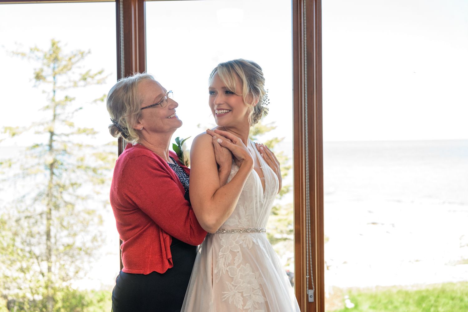 Emotional wedding day moment shared between two people by a window with scenic forest view.