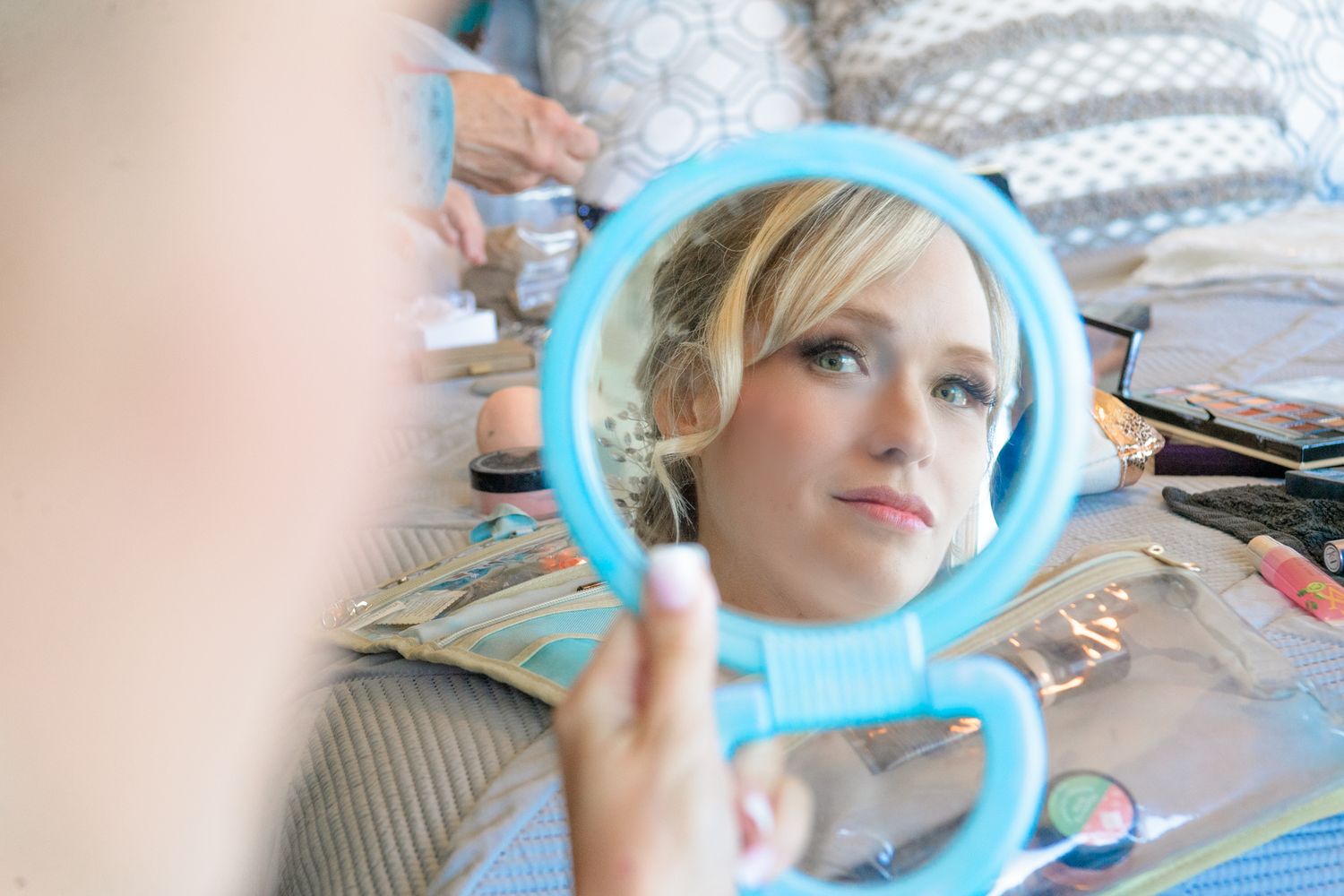 Person looking at reflection in turquoise handheld mirror during wedding preparations.