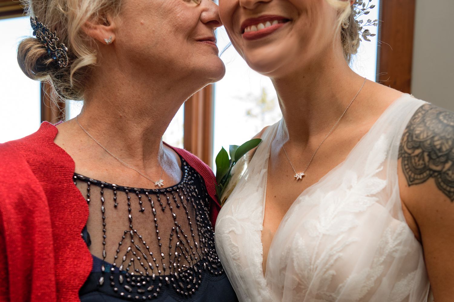 Close-up tender moment between two people, one wearing red cardigan and one in white wedding dress.