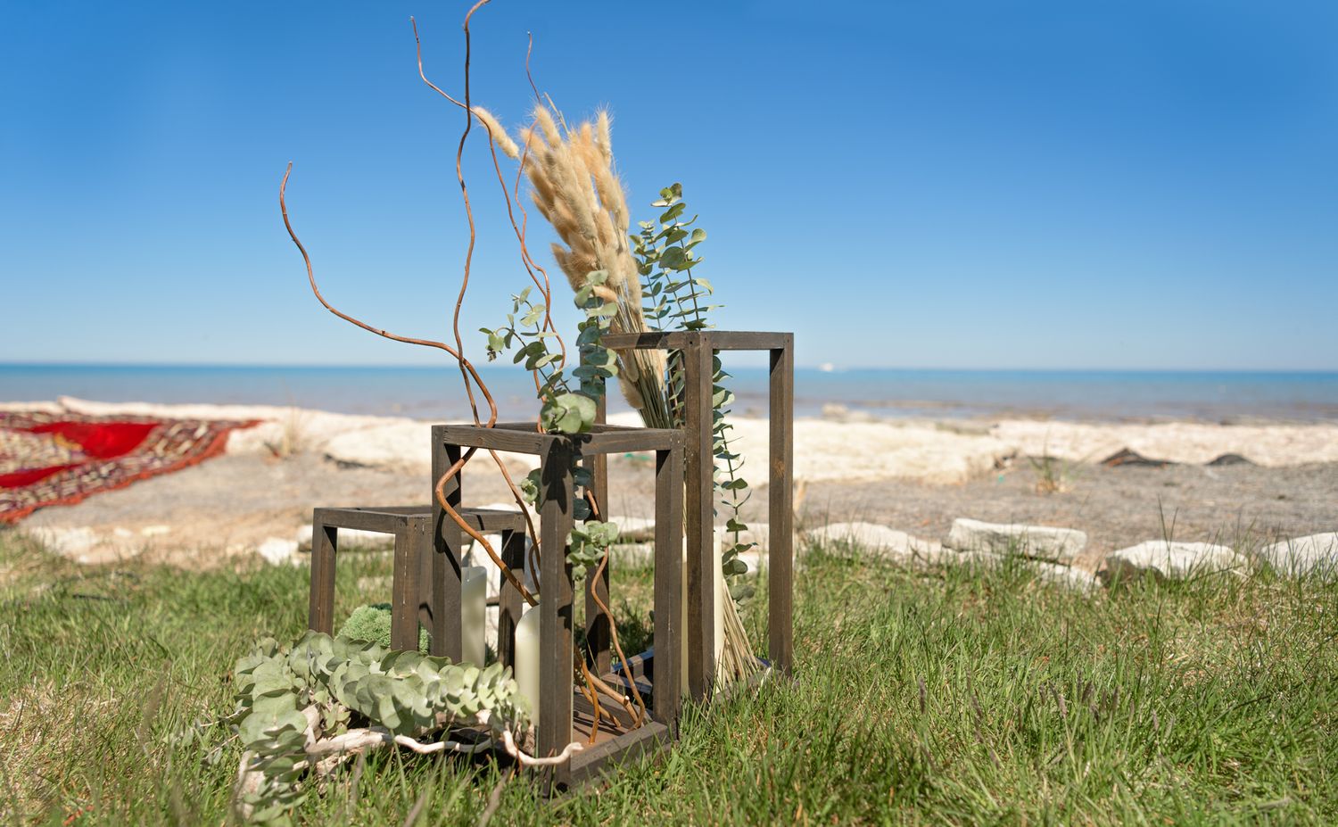 Rustic wooden fence post decorated with dried plants against a beach landscape on a sunny day.