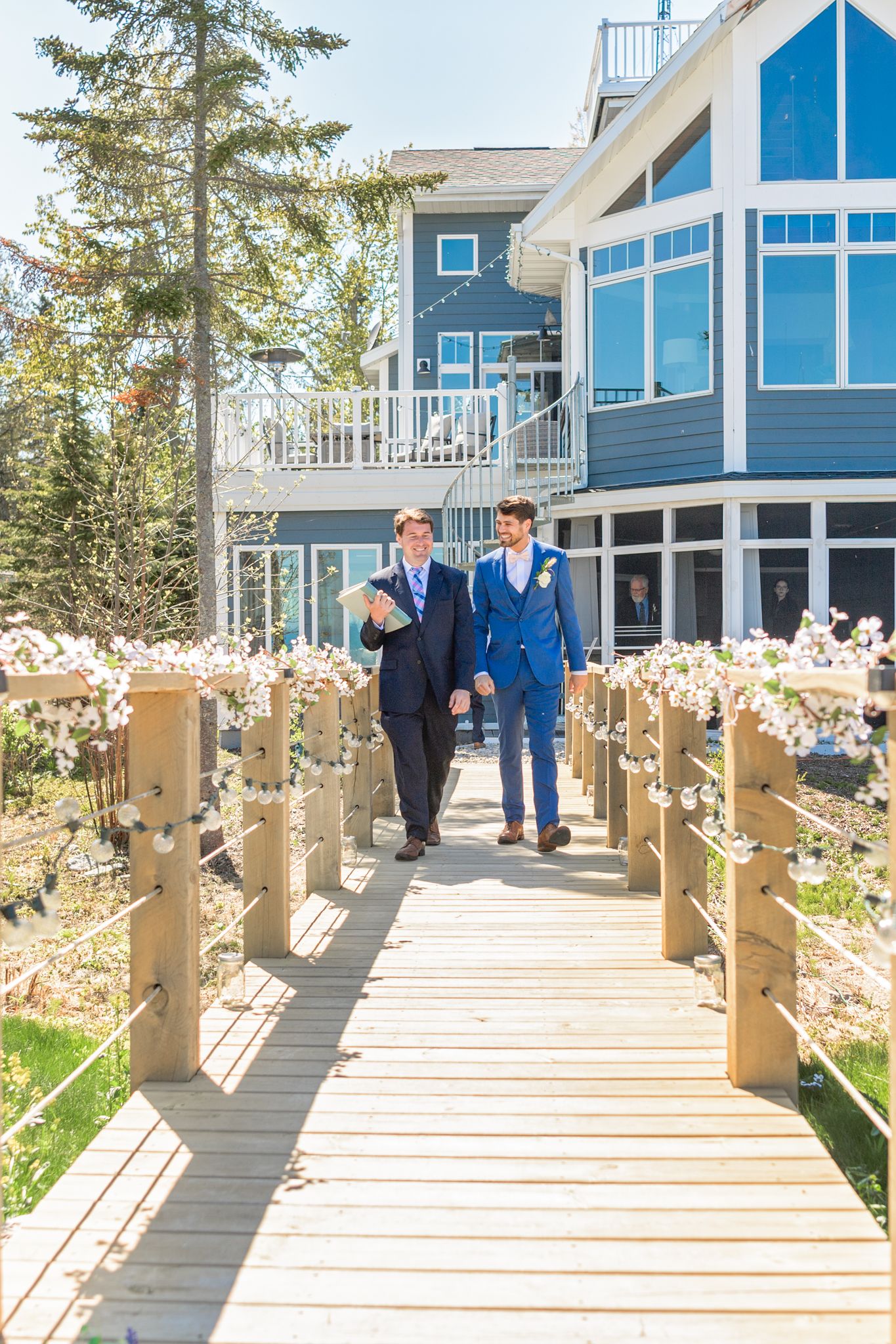 Wooden walkway decorated with floral arrangements leading to a blue coastal house.