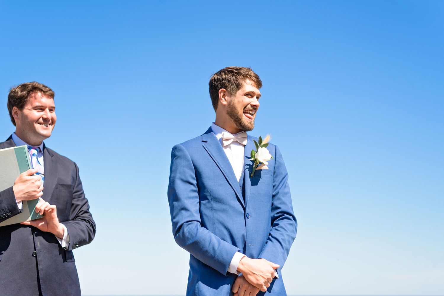 Two people in formal attire standing against bright blue sky during outdoor ceremony.