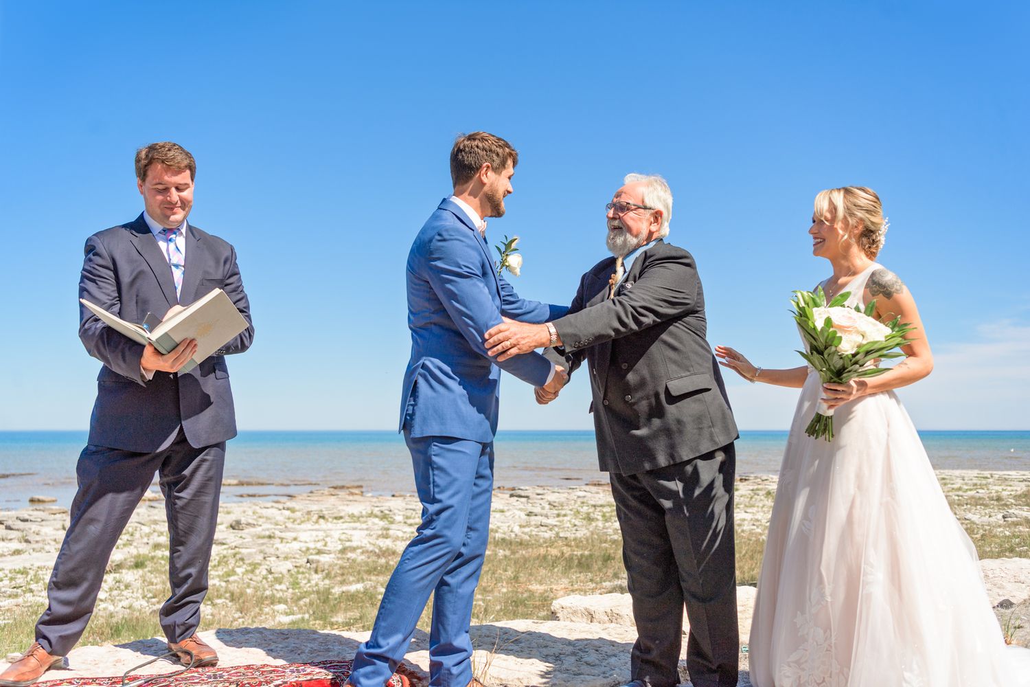 Outdoor wedding ceremony taking place on beach with ocean backdrop.