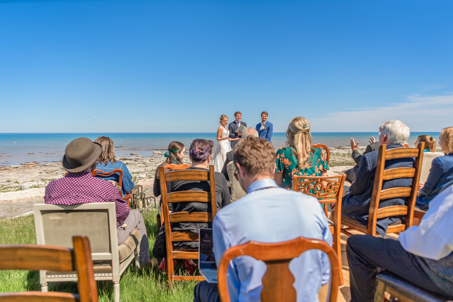 Wedding guests seated in wooden chairs for outdoor ceremony overlooking ocean.