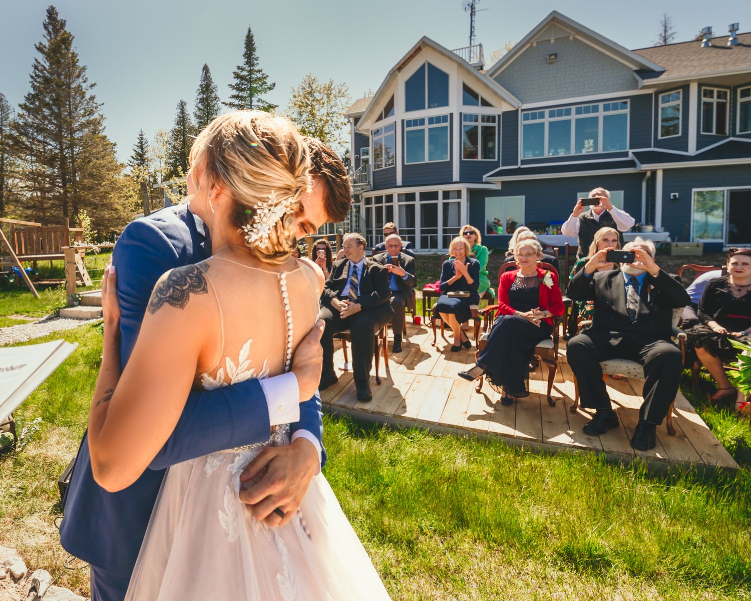 Wedding guests gather outdoors for ceremony in front of waterfront property.