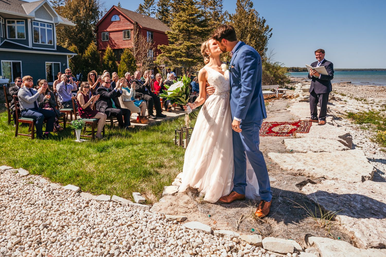 Wedding ceremony by the ocean with guests seated on lawn in front of coastal homes.