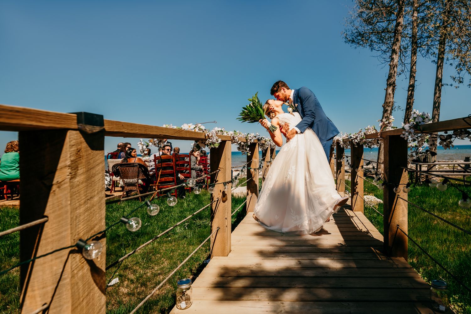 A couple shares a romantic moment on a wooden bridge surrounded by trees and greenery.