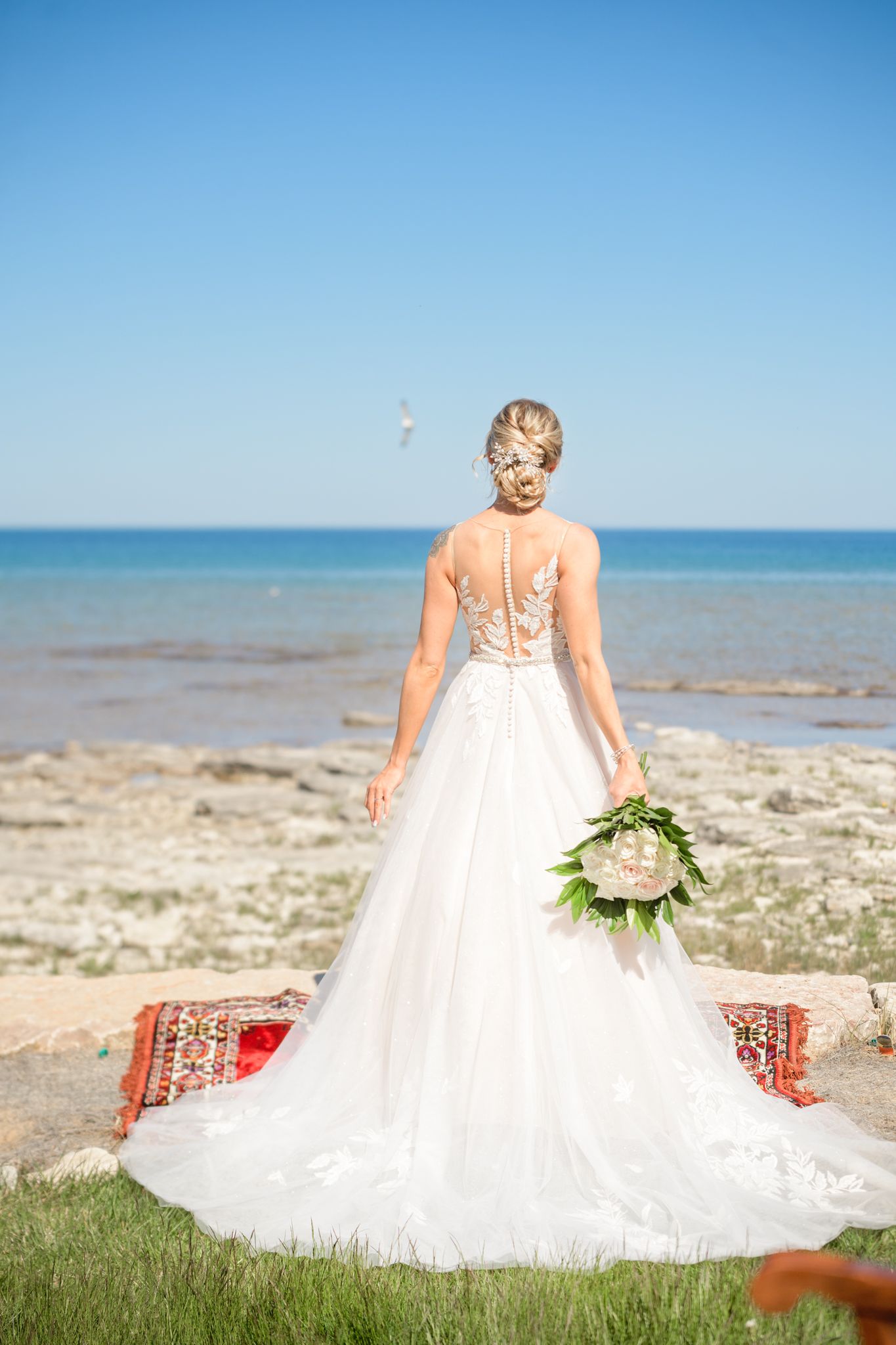 Back view of a wedding dress with delicate lace details and long train on a beach setting.