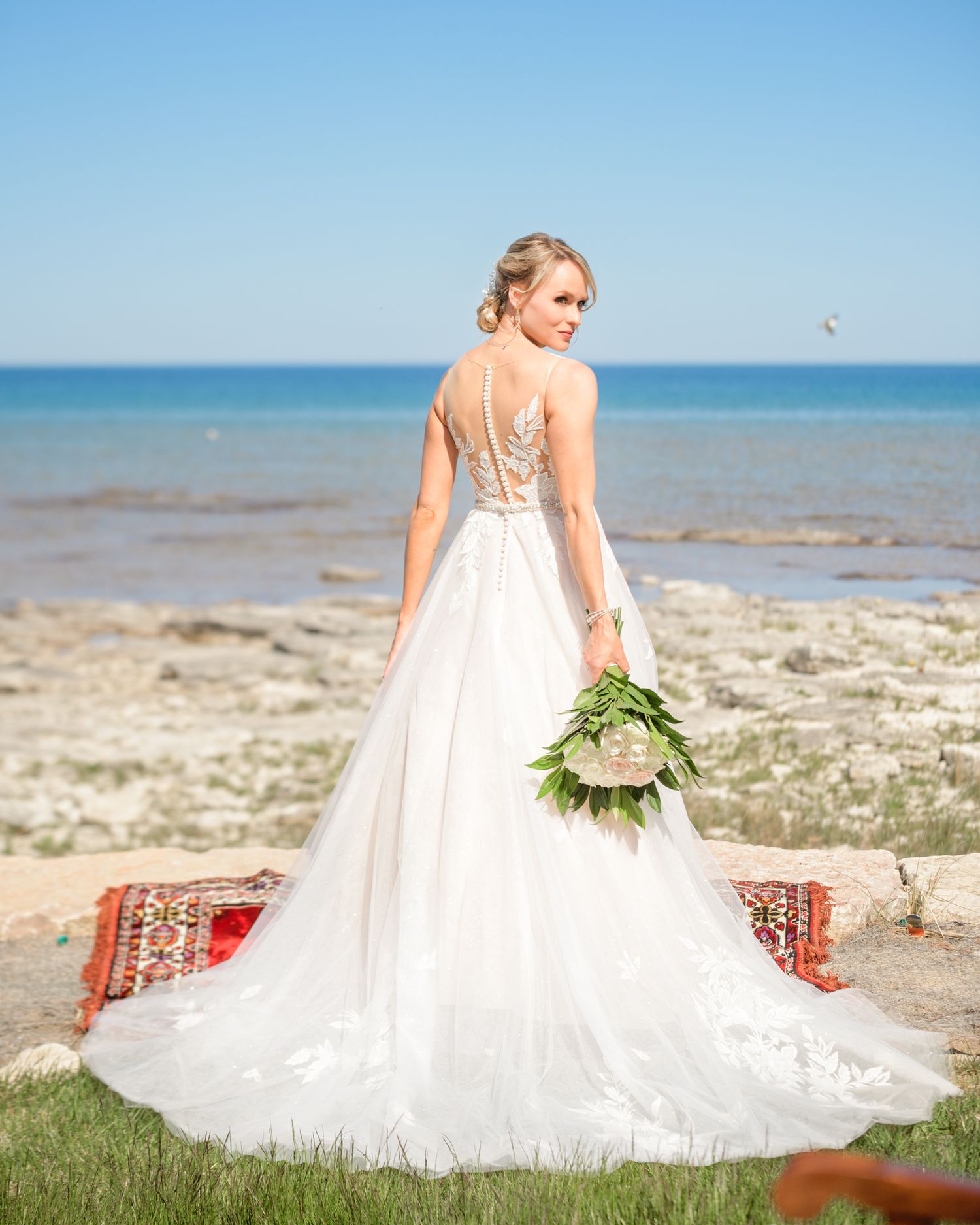 A flowing white wedding dress with intricate back detail captured against a seaside landscape.