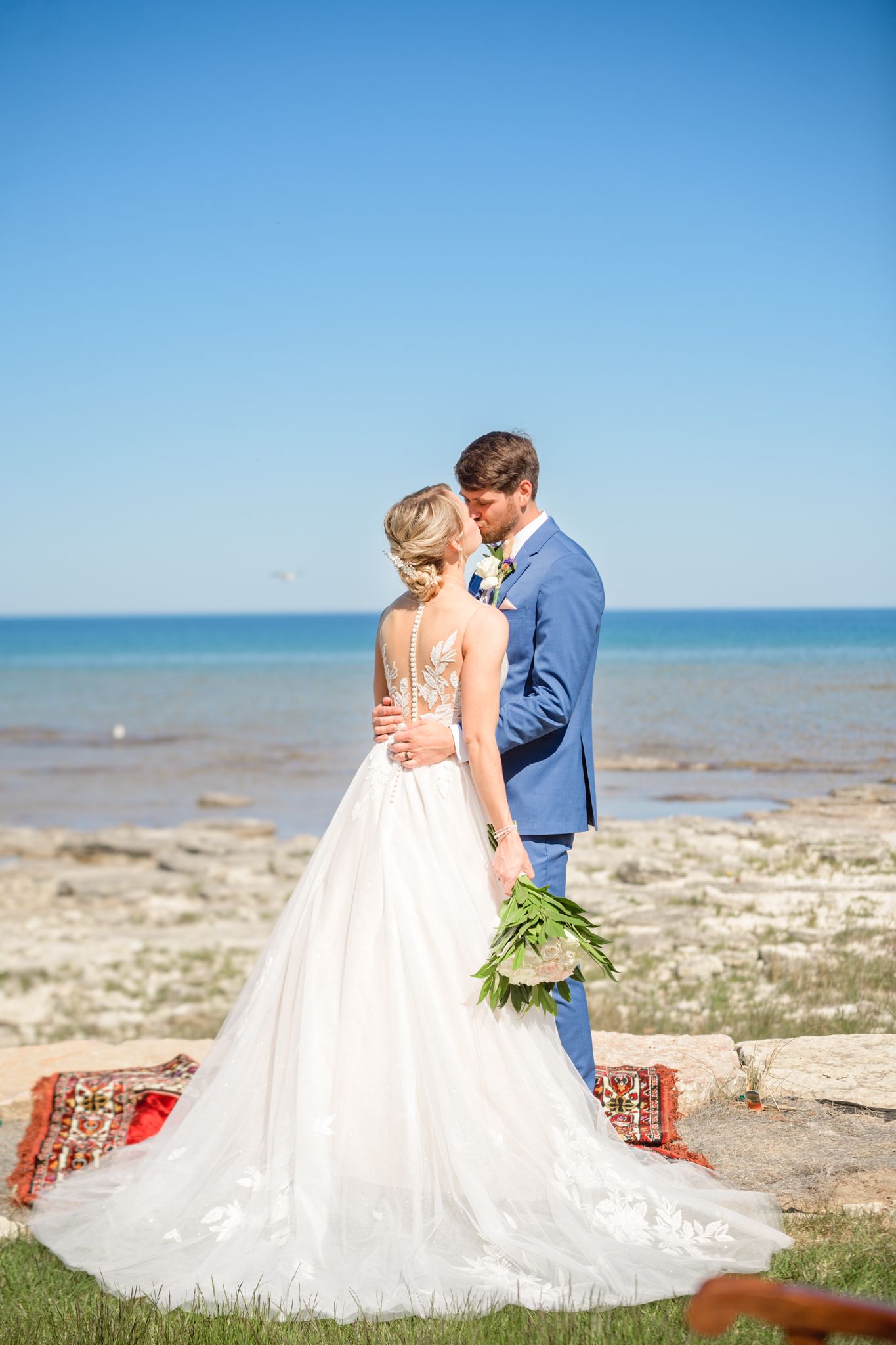 A romantic seaside wedding photo with couple embracing on decorative rug.