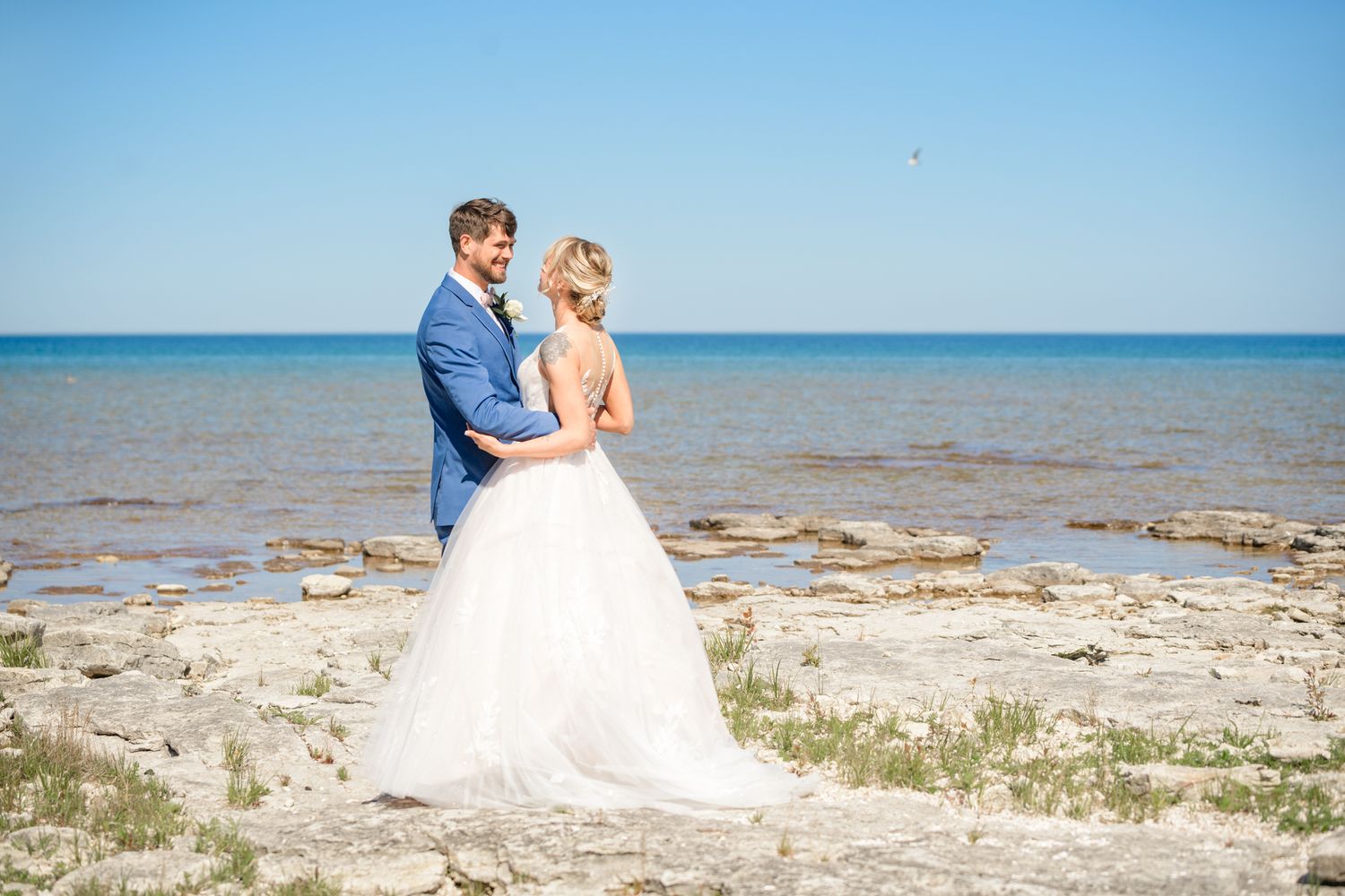 A beautiful wedding photo captured on a rocky beach with the ocean stretching to the horizon.