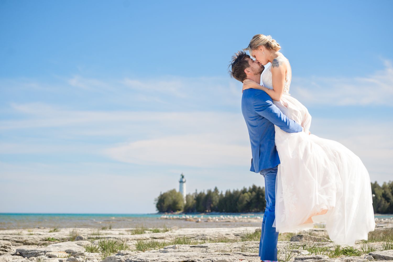 A romantic seaside wedding moment with a lighthouse visible in the background.