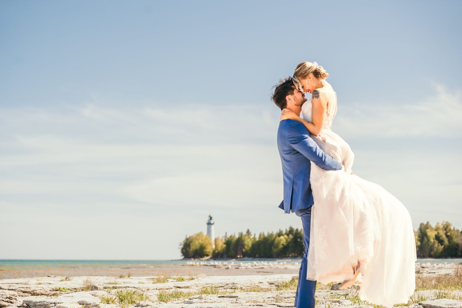 A romantic wedding moment captured against a coastal backdrop with a distant lighthouse.