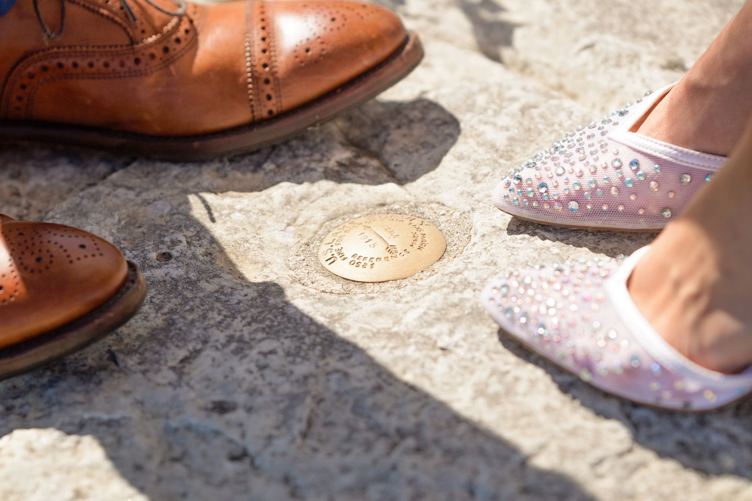 Close-up of wedding shoes showing a brown leather oxford and sparkly bridal flat on stone ground.
