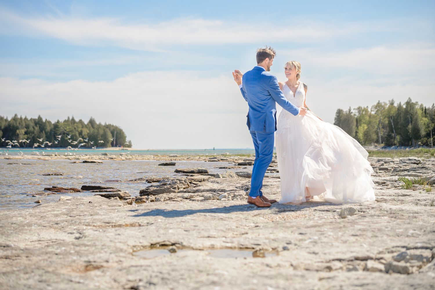 Wedding couple sharing a romantic dance moment on a rocky coastal beach.