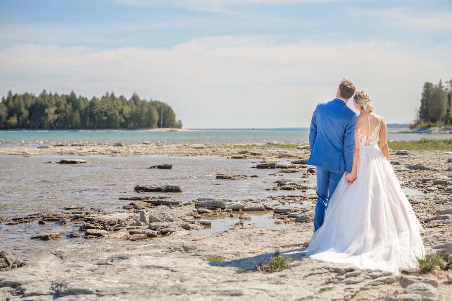 A couple in formal wedding attire overlooking a rocky beach landscape.