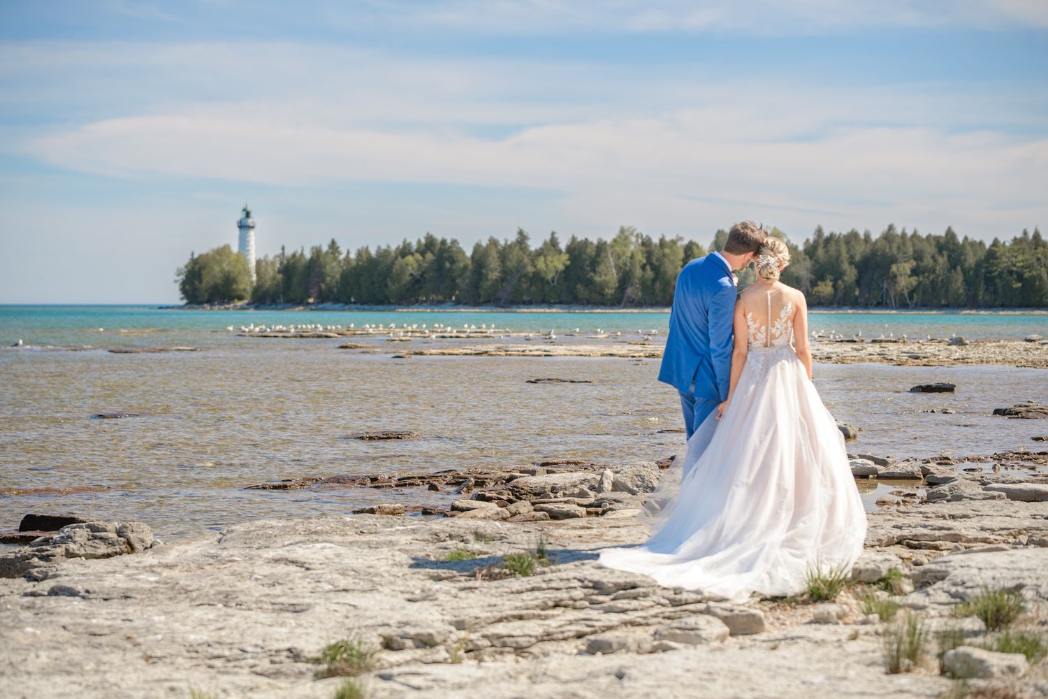 A couple admiring a lighthouse view from a rocky coastal beach.