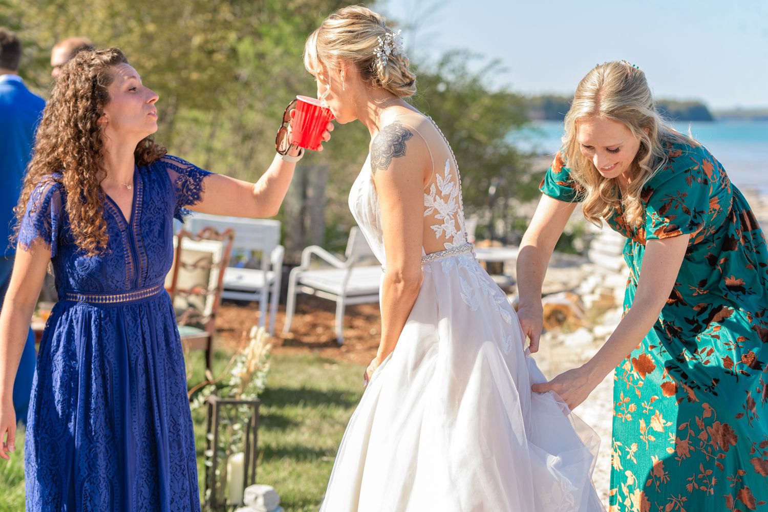 Wedding party members in colorful dresses assist with preparation in an outdoor garden setting.