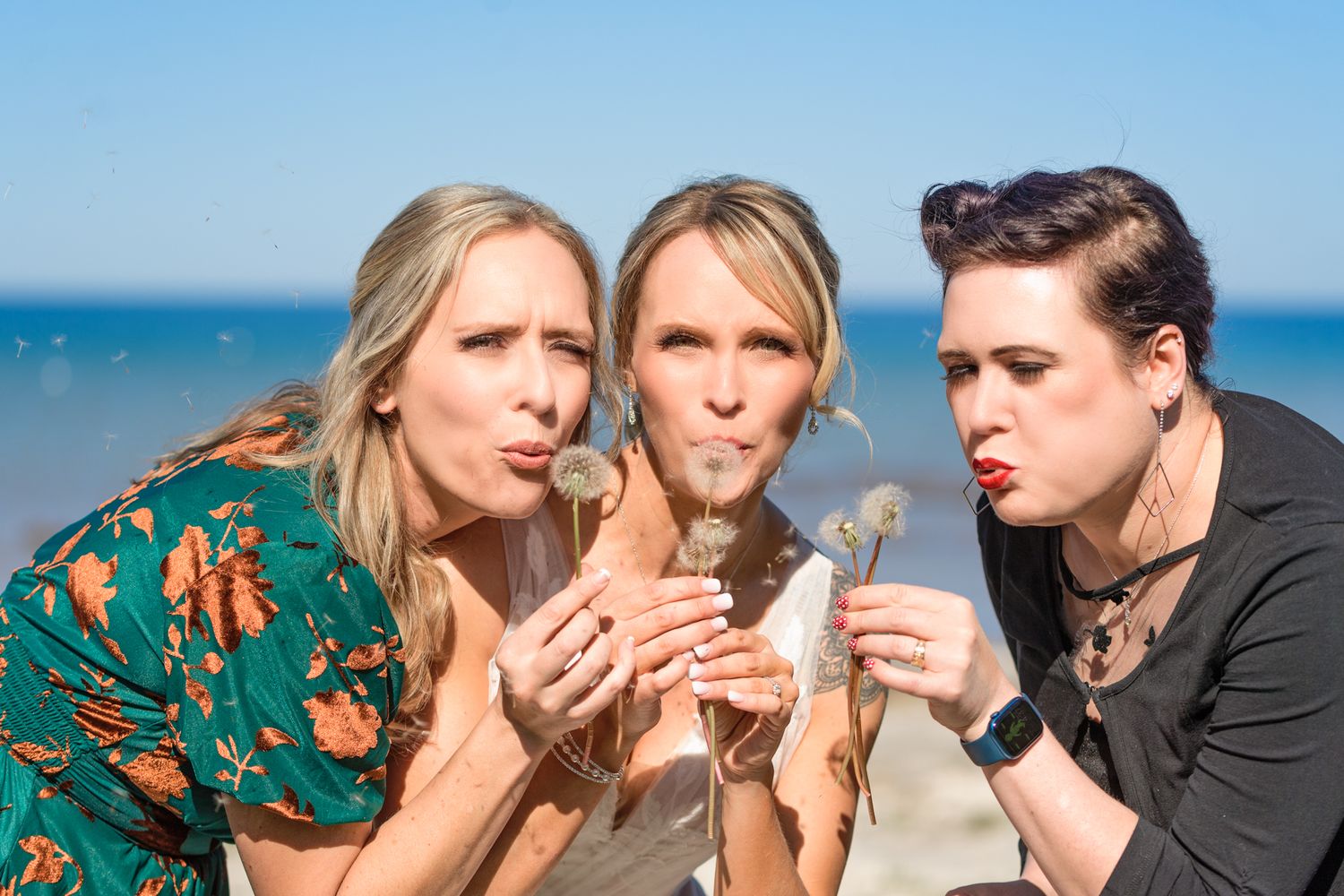 Three wedding party members in colorful attire share a playful moment outdoors.