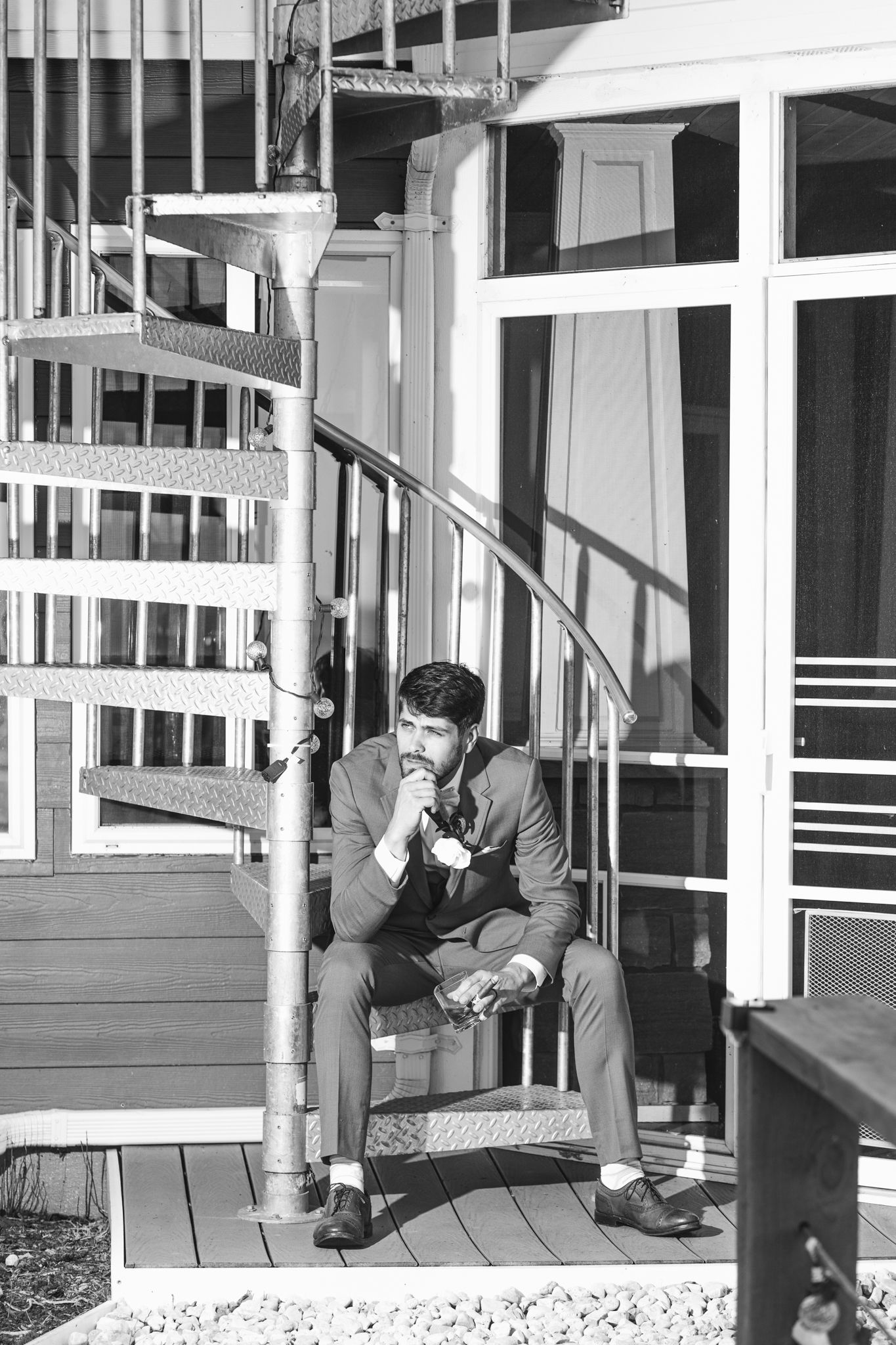 Black and white photo of a person sitting on spiral stairs in a contemplative pose.