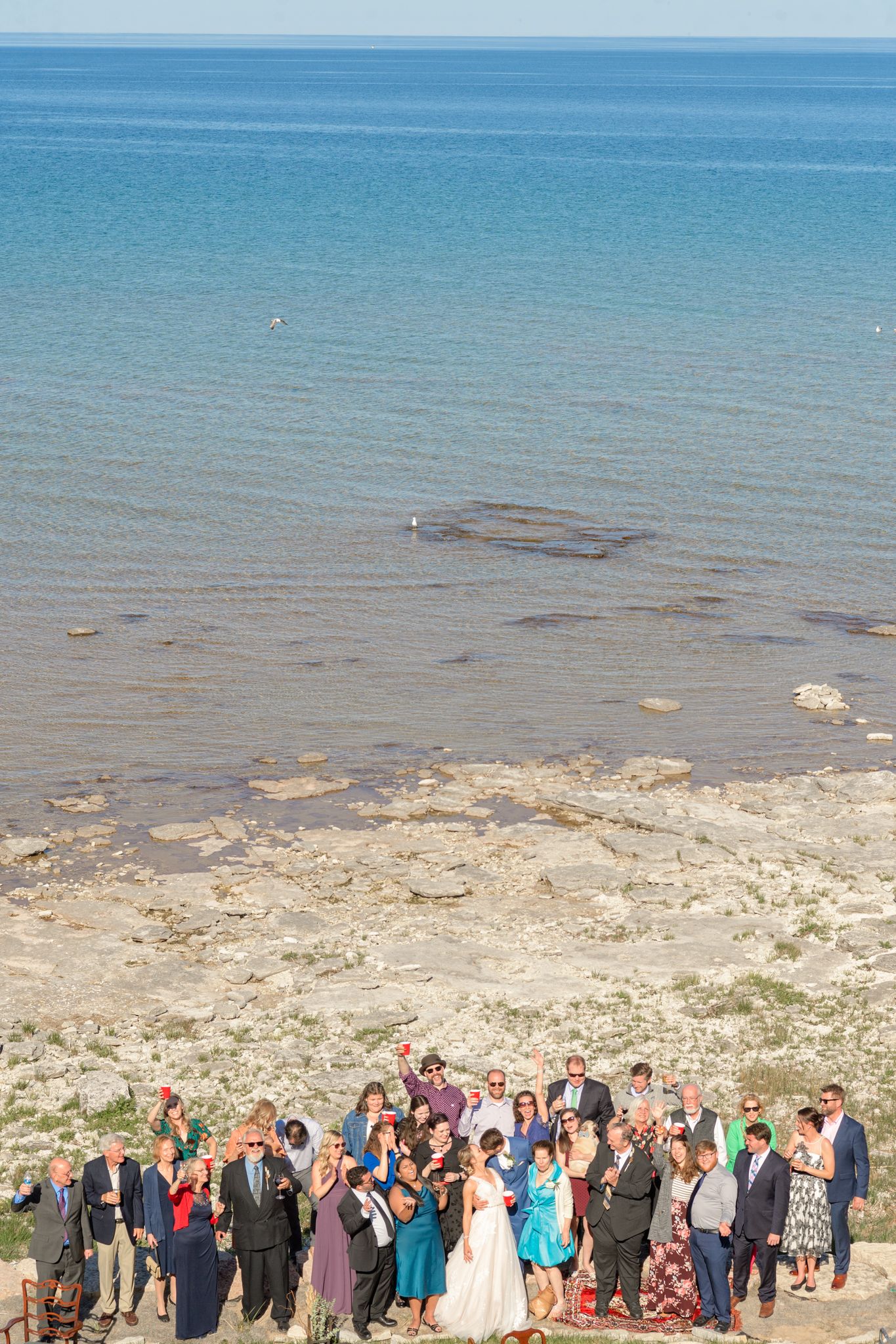 Wedding party and guests gather for a group photo on a scenic coastal cliff overlooking the ocean.