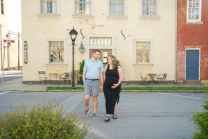 A couple stands together on a historic street with classic architecture in the background.