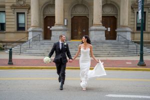 A newlywed couple runs joyfully down courthouse steps holding hands after their wedding ceremony.