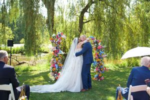 A romantic outdoor wedding ceremony under weeping willow trees with colorful floral arrangements.