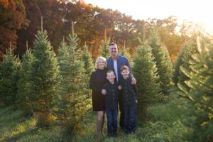 A group stands together among evergreen Christmas trees at a tree farm during golden sunset hour.