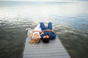 Two people lie on a wooden dock over calm water at sunset.