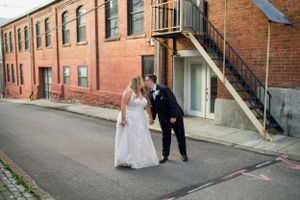 A wedding couple poses on a cobblestone street beside a historic brick building.