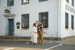 Couple embraces in front of white historic building with blue trim and window boxes on a street corner.